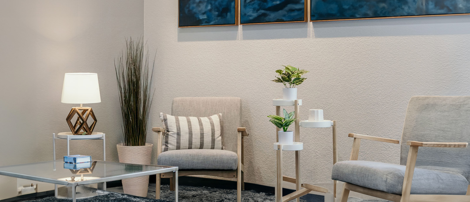 The image shows an interior space with modern furniture including a sofa, chairs, a coffee table, and decorative items such as plants and artwork on the walls.