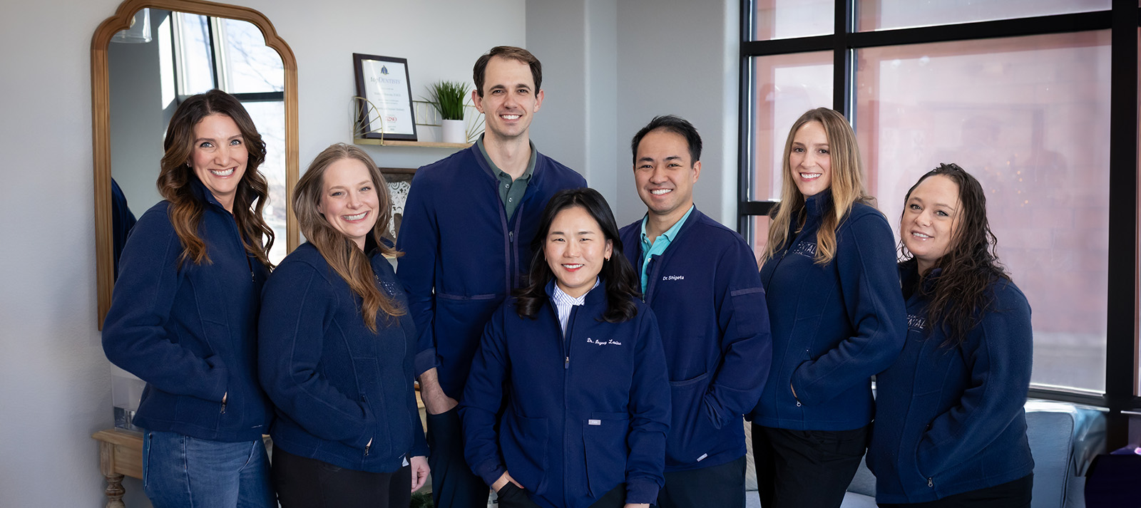 A group of people wearing matching blue jackets posing together in an office setting.