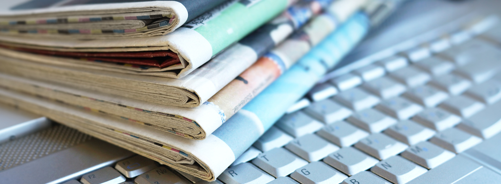The image shows a stack of newspapers with visible headlines on a table.