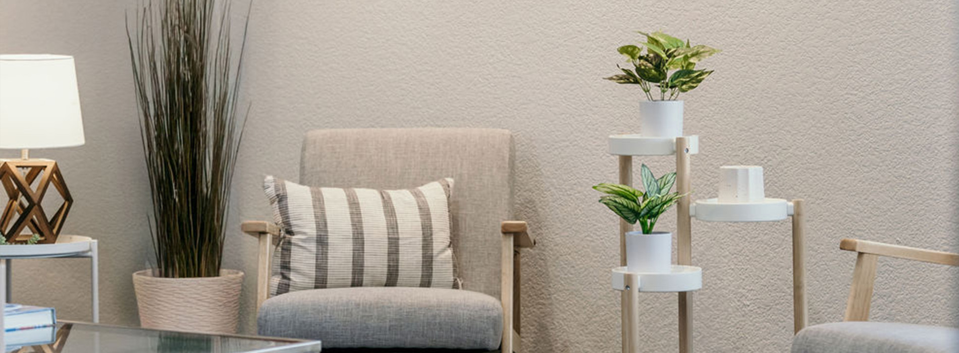 The image shows an interior space with modern furniture, including a couch and chair, placed in front of a wall-mounted plant and a decorative arrangement of cylindrical objects.