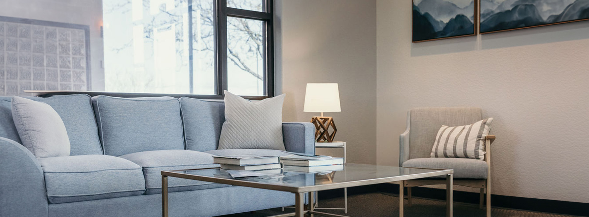 A modern living room setting with a blue sofa, white armchair, coffee table, rug, and framed picture on the wall.