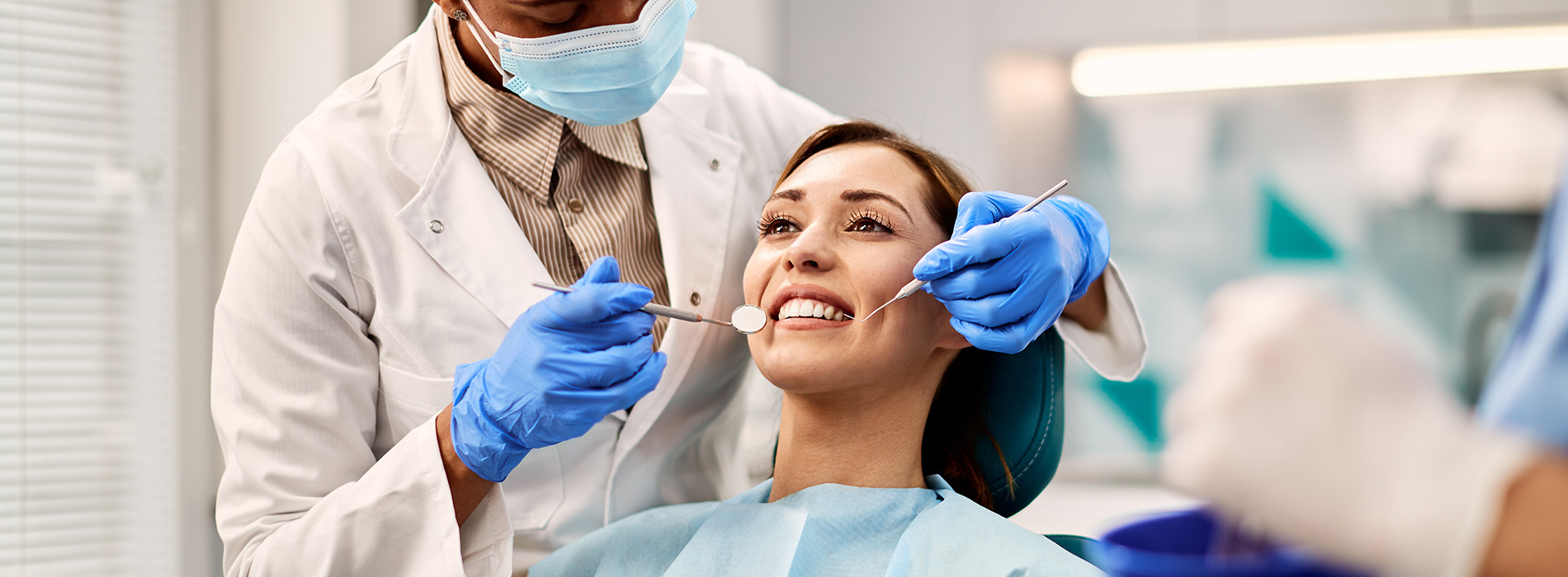 The image shows a dental professional performing a procedure on a patient in a clinical setting, with both individuals wearing protective gloves and masks.