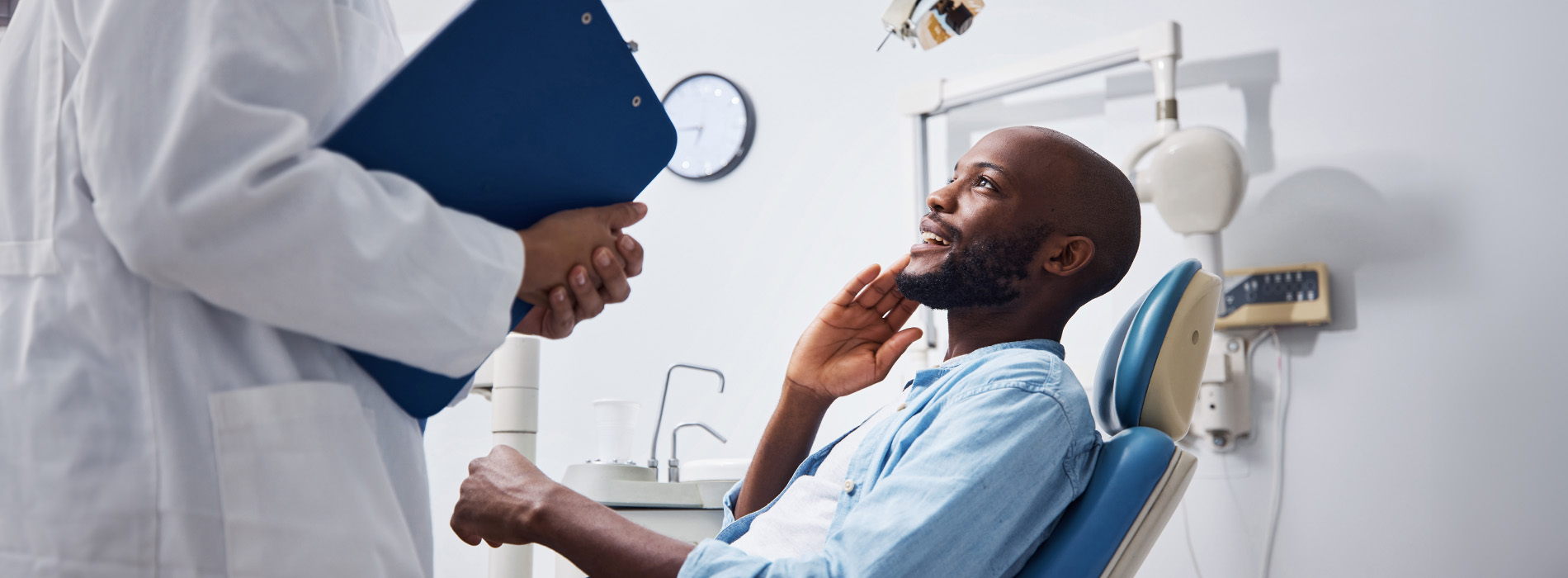 The image shows a dental office setting with a dentist performing an examination on a patient while another person looks on.