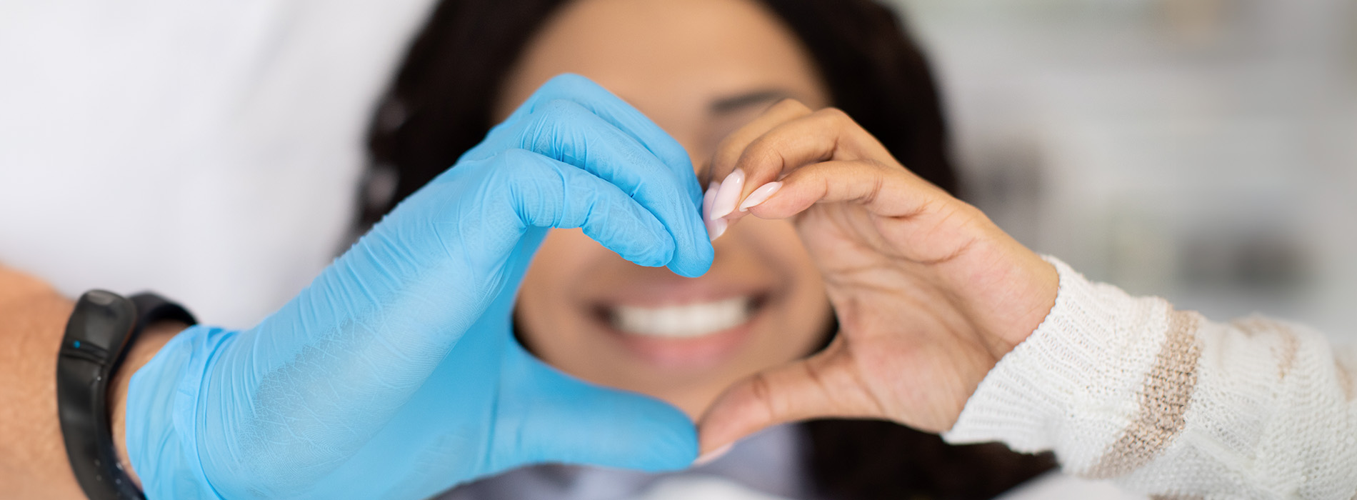 The image shows a person wearing gloves holding up a heart-shaped object with both hands, possibly a medical or healthcare setting.