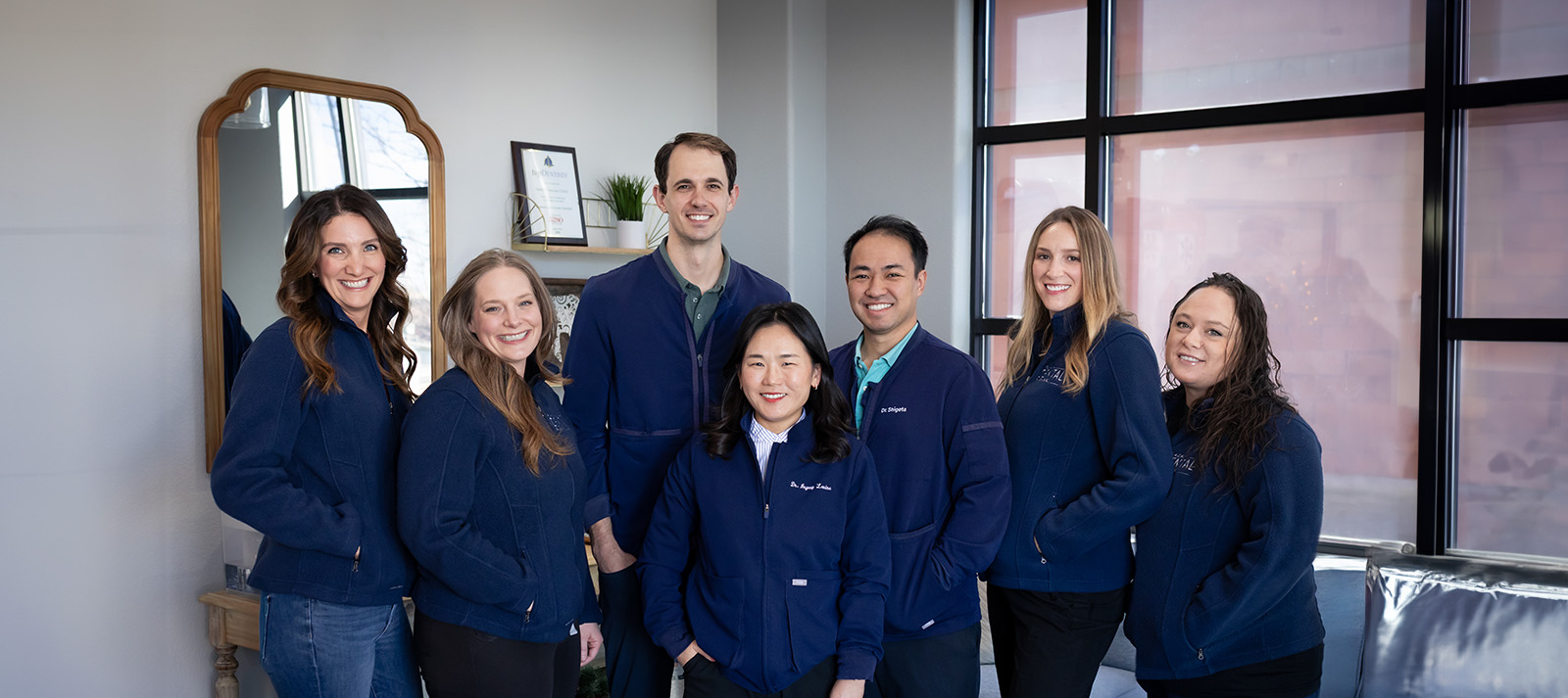 A group of people posing together, likely employees, in front of a building, smiling at the camera.