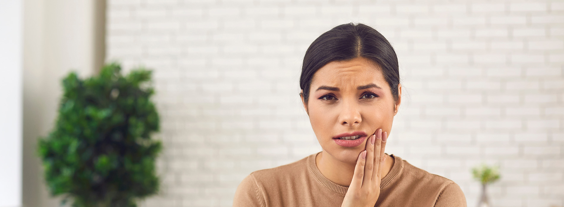 A woman with dark hair is captured mid-motion, brushing her teeth while looking upwards and slightly to the right. She appears surprised or shocked.