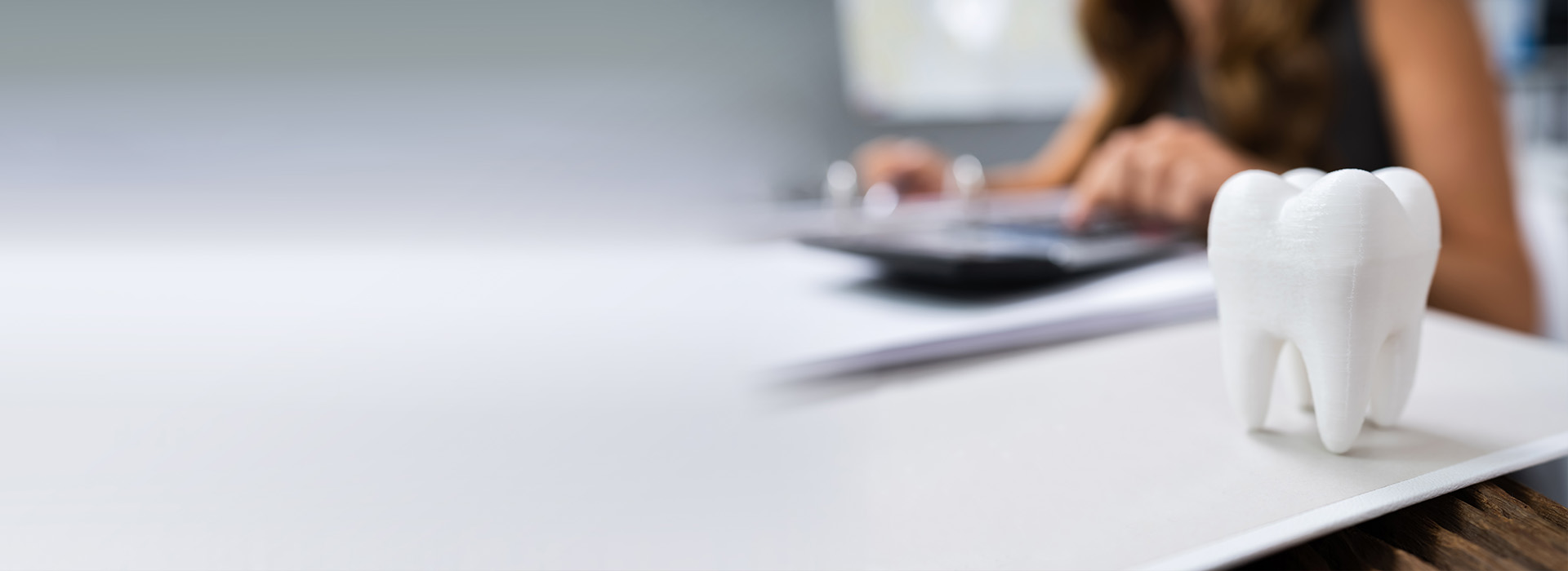 A person sitting at a desk with their back to the camera, working on a laptop, while a white toothbrush rests on the desk.
