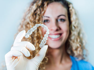 The image shows a person holding up a large dental retainer with a smile.