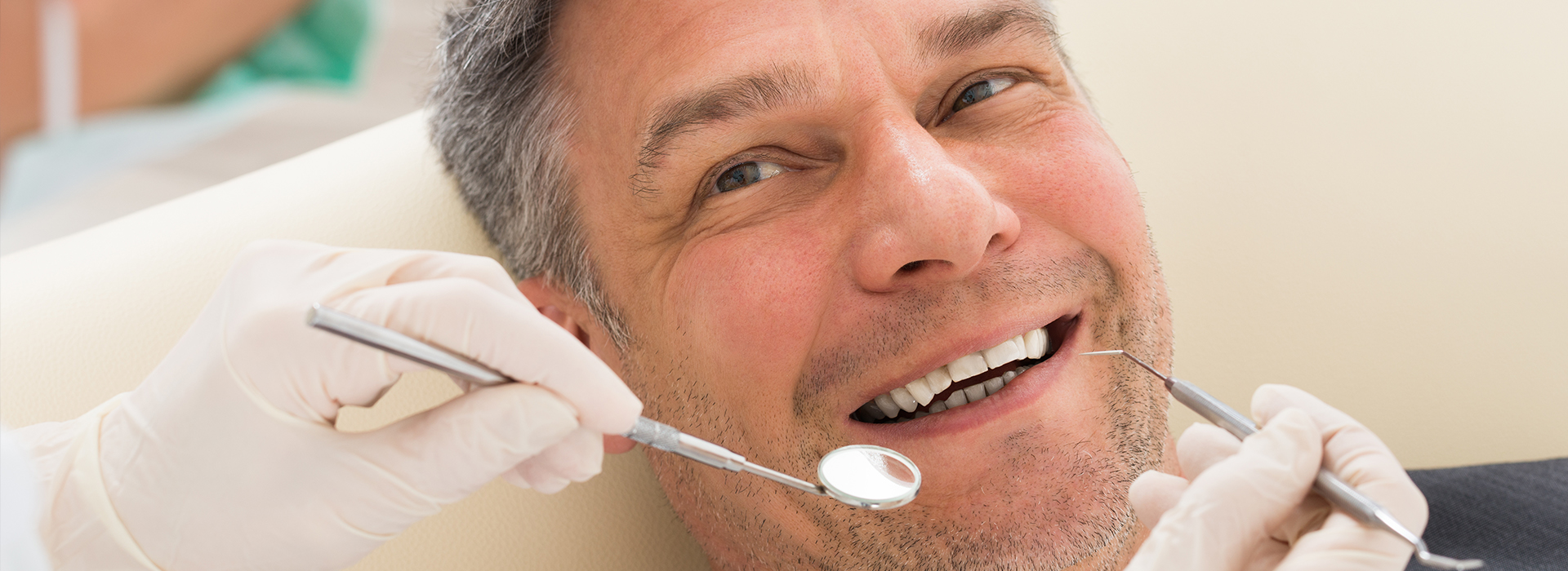 A man sitting in a dental chair with various dental instruments around him, smiling broadly at the camera.