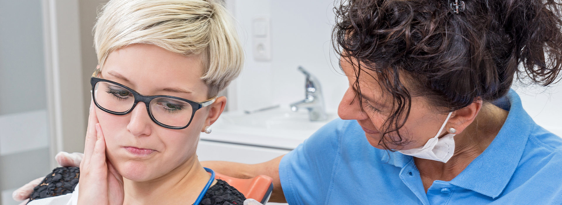 A woman with glasses is sitting in a dental chair receiving care from a female dentist.