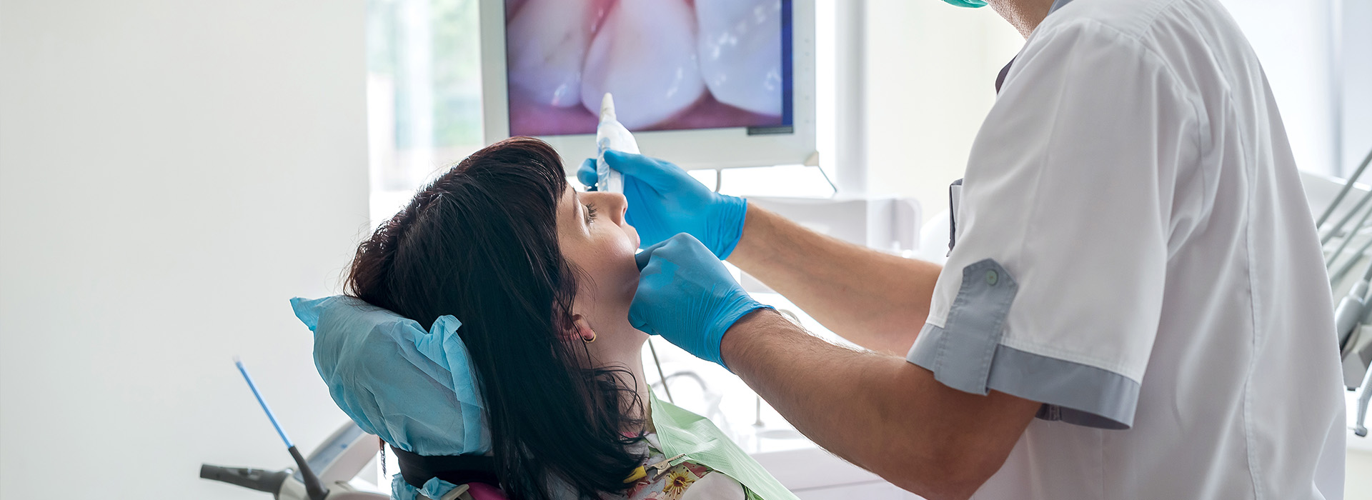 A dental hygienist cleaning teeth at a dental clinic, with a patient seated in the chair.
