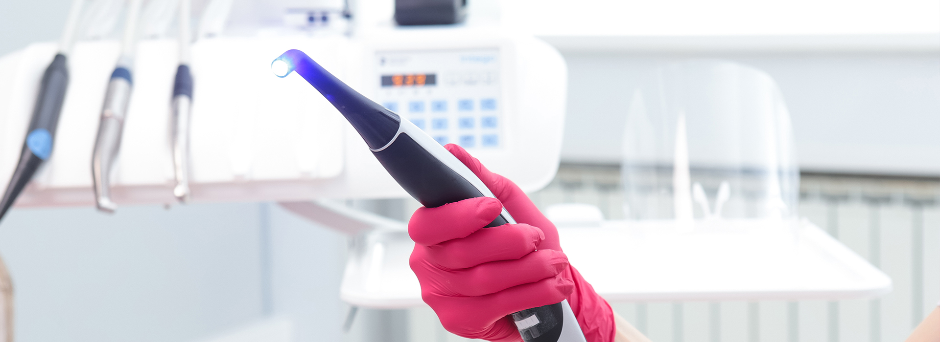 An individual wearing red gloves uses a blue device with a black tip, likely for cleaning or sanitizing purposes, within a professional setting.