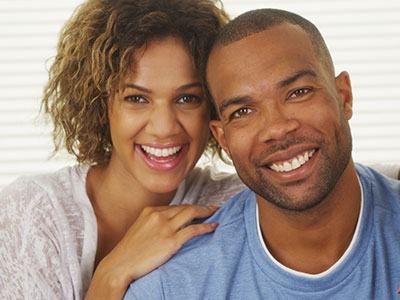 A man and woman smiling at each other with a warm, affectionate expression, posing for a portrait-style photograph.