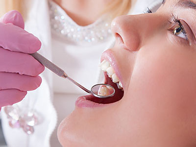 A woman receiving dental care with a professional using a drill on her teeth while wearing a pink mask.