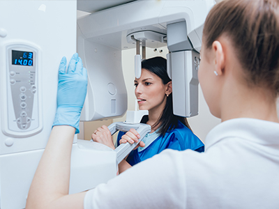 Woman standing next to large 3D scanner, both wearing blue gloves and face masks.