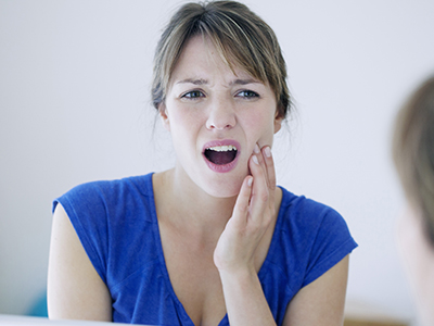 The image shows a woman with her mouth open, looking distressed, with a hand placed on her chin, set against a blurred background.