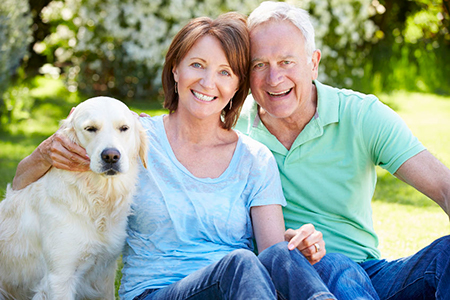 An elderly couple posing with their golden retriever on a grassy lawn.