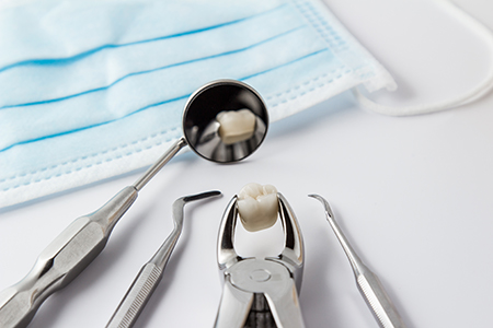 The image shows a collection of dental tools including a toothbrush with toothpaste on it, a dental mirror, a pair of scissors, and a small drill, all placed on a white surface next to a blue cloth.