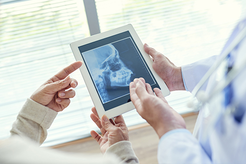 A medical professional holds a tablet displaying an X-ray with another individual looking on.