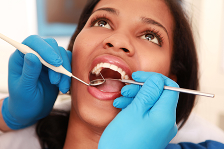 A woman receiving dental care with a dental hygienist performing an oral examination using specialized tools.