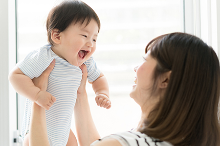 The image shows a woman holding a baby with a joyful expression, looking at the camera while smiling.