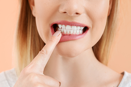 The image shows a person with their finger on their teeth, possibly indicating dental care or oral hygiene, against a plain background.