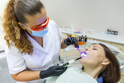 The image depicts a dental hygienist performing a teeth cleaning procedure on a patient who appears to be undergoing cosmetic dentistry, with the hygienist using a dental mirror and a specialized tool to clean the teeth.