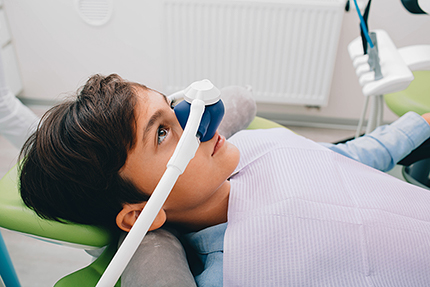 A young boy seated in dental chair with headgear, receiving dental treatment.