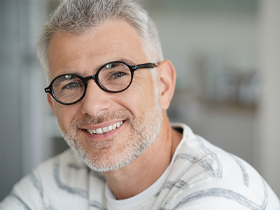 The image shows a man with glasses smiling at the camera, appearing relaxed and contented.