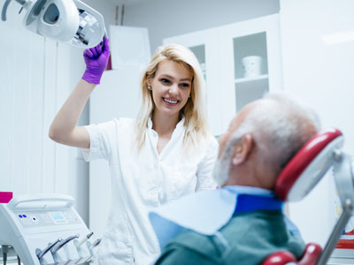Woman standing in front of man sitting in dental chair with open mouth.