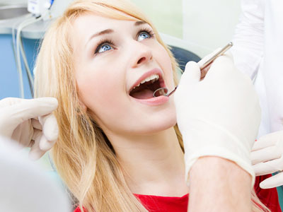 A woman receiving dental treatment with a dentist performing the procedure, surrounded by medical equipment and personnel.