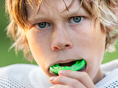 The image shows two photos of a young boy with blonde hair holding a green object, possibly a toothbrush, to his mouth, with one photo showing him with his teeth uncovered and the other with them covered by the green object.