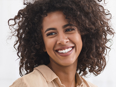 The image shows a smiling woman with curly hair wearing a white top, appearing to be indoors against a light background.