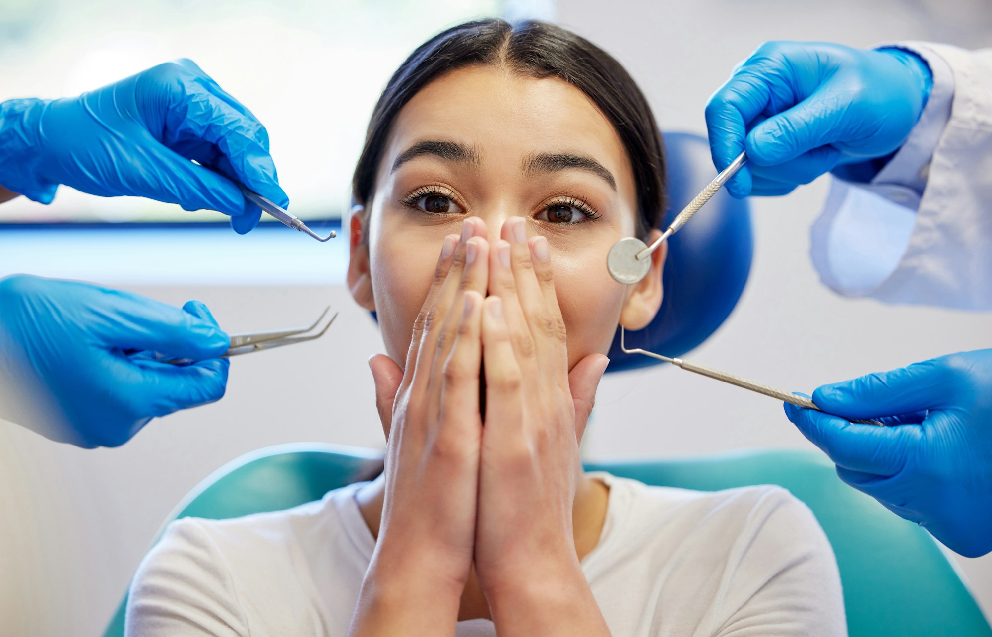 Young girl covering her mouth in fear as gloved hands with dental tools approach, representing dental anxiety and the availability of sedation dentistry at Plaza Dental Parker.